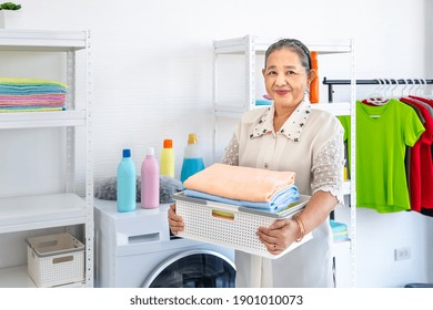 Happy Smiling Asian Senior Elderly Female Woman Carrying Clothe Basket Doing Laundry With Washing Machine, House Cleaning And Housekeeping, Looking At Camera