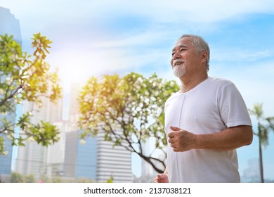 Happy And Smiling Asian Senior Man Doing Exercise And Jogging Or Walking With Relaxation For Healthy In Park Outdoor After Retirement During Summer Time. Health Care Elderly Outdoor Lifestyle Concept.