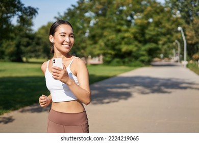 Happy smiling asian woman jogging in park. Healthy young female runner doing workout outdoors, running on streets. - Shutterstock ID 2224219065
