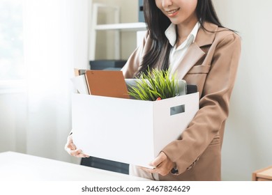 Happy smiling asian young business woman office worker celebrating resignation, holding belongings into cardboard box leaving office after quitting job, change position, leaves the company, leave job - Powered by Shutterstock