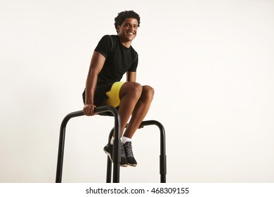 Happy Smiling Attractive African American Man In Black Synthetic Workout Gear Exercising At Home On Parallel Bars, Isolated On White