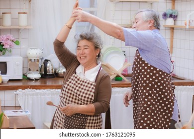 Happy & smiling attractive elderly cute Asian couple in love enjoying cooking healthy salad & dancing in kitchen at home together. Happiness family of beautiful romantic married lover relationship