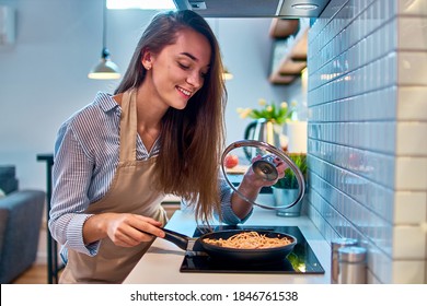 Happy smiling attractive young cooking woman housewife preparing food in a frying pan on the stove for delicious dinner at modern loft style kitchen   - Powered by Shutterstock