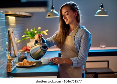 Happy lächelnde attraktive junge Hausfrau, die mit einem elektrischen Wasserkocher zum Kaffee-Abend Pause in der modernen Loft-Küche
