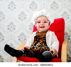 Happy Smiling Baby Girl Sitting In A Chair. Wearing Granny Costume With Glasses.