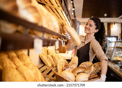 Happy smiling bakery worker placing loaf of bred on the shelf ready for sale. - Powered by Shutterstock