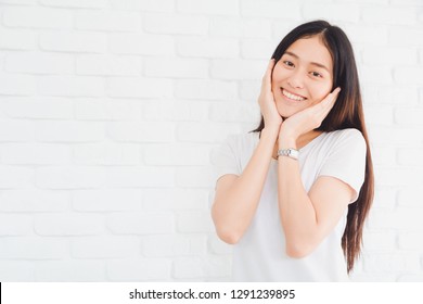 Happy Smiling Beautiful Asian Woman Gesturing With Hands And Showing Two Hands Touch On Her Face In A White Brick Wall Background.Concept Of Healthy And Beauty Lifestyle Girl.