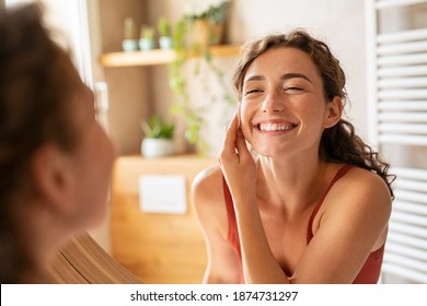 Happy smiling beautiful girl cleaning skin face with cotton pad. Beauty natural woman looking in mirror while cleansing skin face and using cosmetic products for properly deep clean.