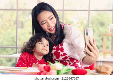 Happy Smiling Beautiful Young Asian Mom Holding Mobile Phone Taking Selfie With Her Little Adorable Child Daughter Girl, Mother Enjoy Spending Special Time With Her Kid. Love And Warmth Family Concept