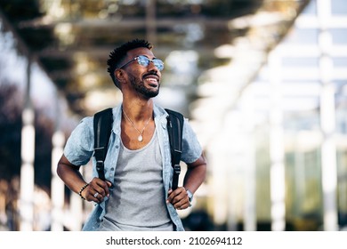 Happy and smiling black man with glasses and backpack walking down the street. Taking the handles of the backpack with his hands. - Powered by Shutterstock