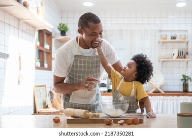 Happy smiling Black son touching his father face with flour while doing bakery at home, Cheerful African American family cooking baking cake or cookie in the kitchen - Powered by Shutterstock