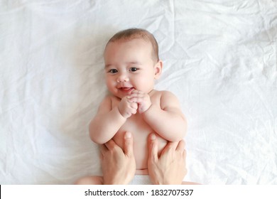 Happy smiling boy belly massaging by his mother at home. Mixed race Asian-German newborn relaxing baby massage top view.