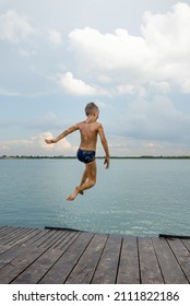 Happy smiling boy enjoying summer vacation on the beach. Jumping to the water of lake.
