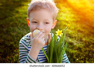 happy smiling boy holding easter egg in hand enjoying beautiful blooming flowers in the park