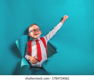 Happy smiling boy in uniform break blue paper wall. Kid in glasses go back to school. Success, motivation, winner, genius concept. Businessman looking through hole in paper wall with superman hand - Powered by Shutterstock