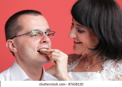 Happy smiling bride and groom young happy couple playfully eating cake on red background