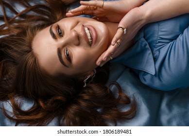 Happy Smiling Brunette Woman Laying On Blue Silk Sheets