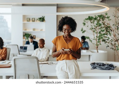 Happy, smiling business woman stands in a modern office, using her smartphone for work. With her glasses on, she looks professional and confident, embodying a young, modern professional woman. - Powered by Shutterstock