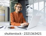 Happy and smiling businesswoman typing on laptop, office worker with glasses happy with achievement results, at work inside office building