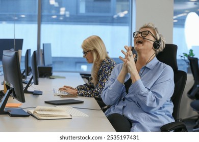 Happy smiling businesswomen with headset sitting with hands clasped at desk in modern office - Powered by Shutterstock