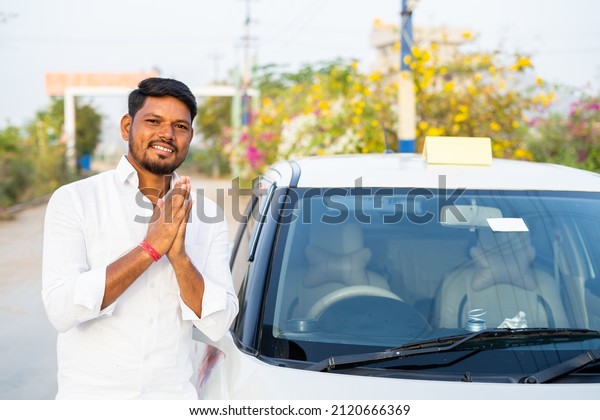 Happy smiling cab driver\
greeting by doing namaste in front of car by looking at camera -\
concept of welcoming passenger, transportation service and self\
employment