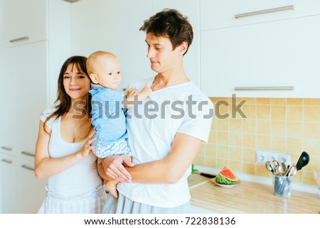 Happy smiling caucasian family with infant boy in sleepwear posing over white kitchen interior.