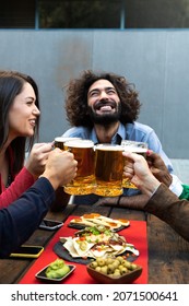 Happy And Smiling Caucasian Man Toasting With Friends With Beer In A Bar Outdoors. Celebratory Toast. Vertical Image.