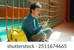 Happy smiling Caucasian teen boy student guy teenager man male son pupil in university school corridor sport hall sitting on floor chatting mobile phone browsing smartphone social media gadget addict