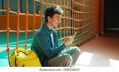 Happy smiling Caucasian teen boy student guy teenager man male son pupil in university school corridor sport hall sitting on floor chatting mobile phone browsing smartphone social media gadget addict - Powered by Shutterstock