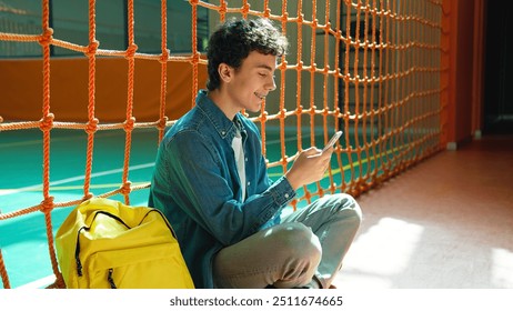 Happy smiling Caucasian teen boy student guy teenager man male son pupil in university school corridor sport hall sitting on floor chatting mobile phone browsing smartphone social media gadget addict - Powered by Shutterstock