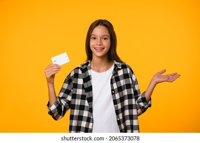 Happy smiling caucasian teenager schoolkid girl pupil student holding credit card for e-banking, online shopping, paying bills isolated in yellow background.