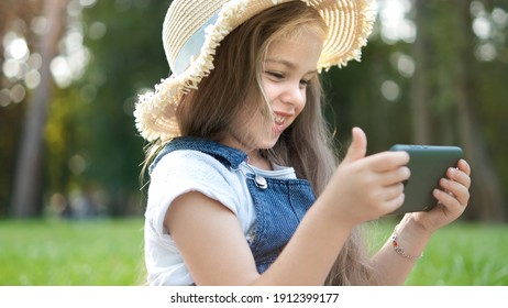 Happy Smiling Child Girl Watching In Her Mobile Phone Outdoors In Summer.