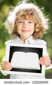 Happy Smiling Child Holding Tablet PC With Ebook Against Green Spring Background. Education Technology Concept