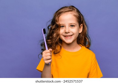 Happy smiling child kid curly hair girl in orange t-shirt brushing teeth with toothbrush on lilac background. Health care, dental hygiene. Mockup, copy space. - Powered by Shutterstock