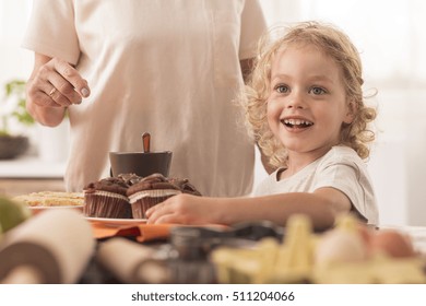 Happy and smiling child willing to eat the muffin from the kitchen worktop