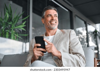 Happy smiling confident mid aged business man, mature professional businessman sitting in outdoor office holding smartphone using mobile phone digital tech looking away thinking. Authentic shot - Powered by Shutterstock