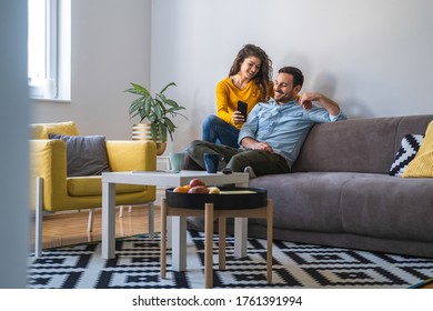 Happy Smiling Couple Embracing And Looking At Smart Phone At Home Stock Photo