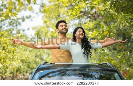 Happy smiling couple feeling nature fresh air by stretching arms on car sunroof - concept of togetherness, weekend holidays and refreshment