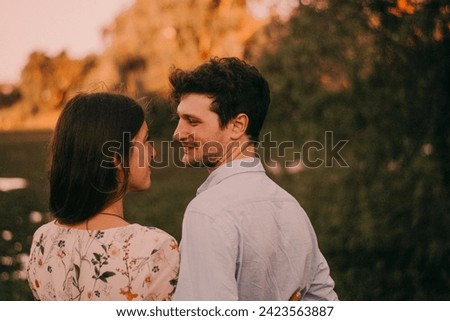 Happy, smiling couple in a green park with the sunset light, hugging, kissing, walking hand in hand, and lying on the ground and grass, representing their love outdoors and sincere love