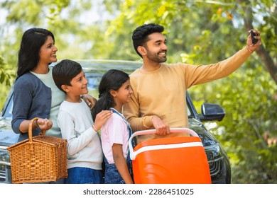 Happy smiling couple with kids taking selfie on mobile phone during summer camp picnic in front of car - concept of family trip, weekend holidays and togetherness. - Powered by Shutterstock