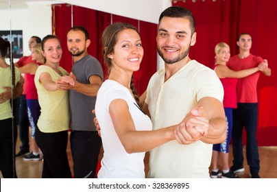 Happy Smiling Couple Learning To Dance Waltz In Dancing School With Other Dancing Pairs In Background