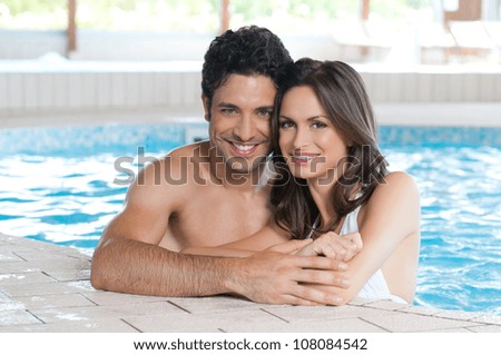 Happy smiling couple looking at camera while relaxing on the edge of a swimmingpool