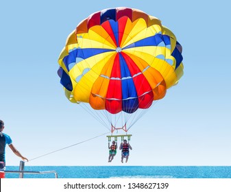 Happy smiling couple Parasailing on Tropical Beach in summer. Newlyweds under parachute hanging mid air. Having fun. Tropical Paradise. Positive human emotions.