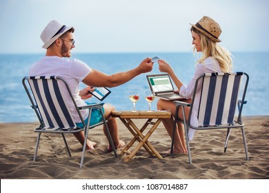 Happy smiling couple surfing the net and enjoy the summer at tropical beach using laptop, digital tablet and credit card - Powered by Shutterstock