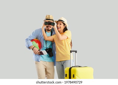 Happy smiling couple tourist looking forward through binocular studio shot portrait. Man and woman lovers in summer hat with luggage suitcase, beach accessory, flight ticket and funny crazy expression