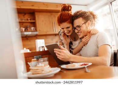 Happy smiling couple using tablet together at kitchen table - Powered by Shutterstock