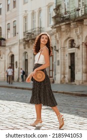Happy smiling curly brunette woman wearing trendy summer outfit walking in street of European city. Fashion, lifestyle conception. Full-length outdoor portrait