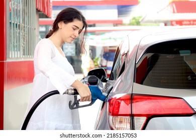 Happy smiling customer woman standing and waiting for filling up her car with fuel petrol pump nozzle against, beautiful young lady traveler self refueling car with petrol at self-service gas station.