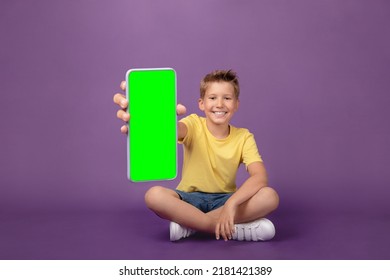 Happy Smiling Cute Kid Boy Showing Cell Phone With Green Screen Chroma Key And Looking At Camera. Indoor Studio Shot Purple Background 