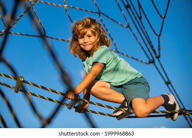 Happy Smiling Cute Little Child Boy Play Monkey Bars On The Web In Outdoor Playground. Kids In Rope Park. Funny Kids Face.